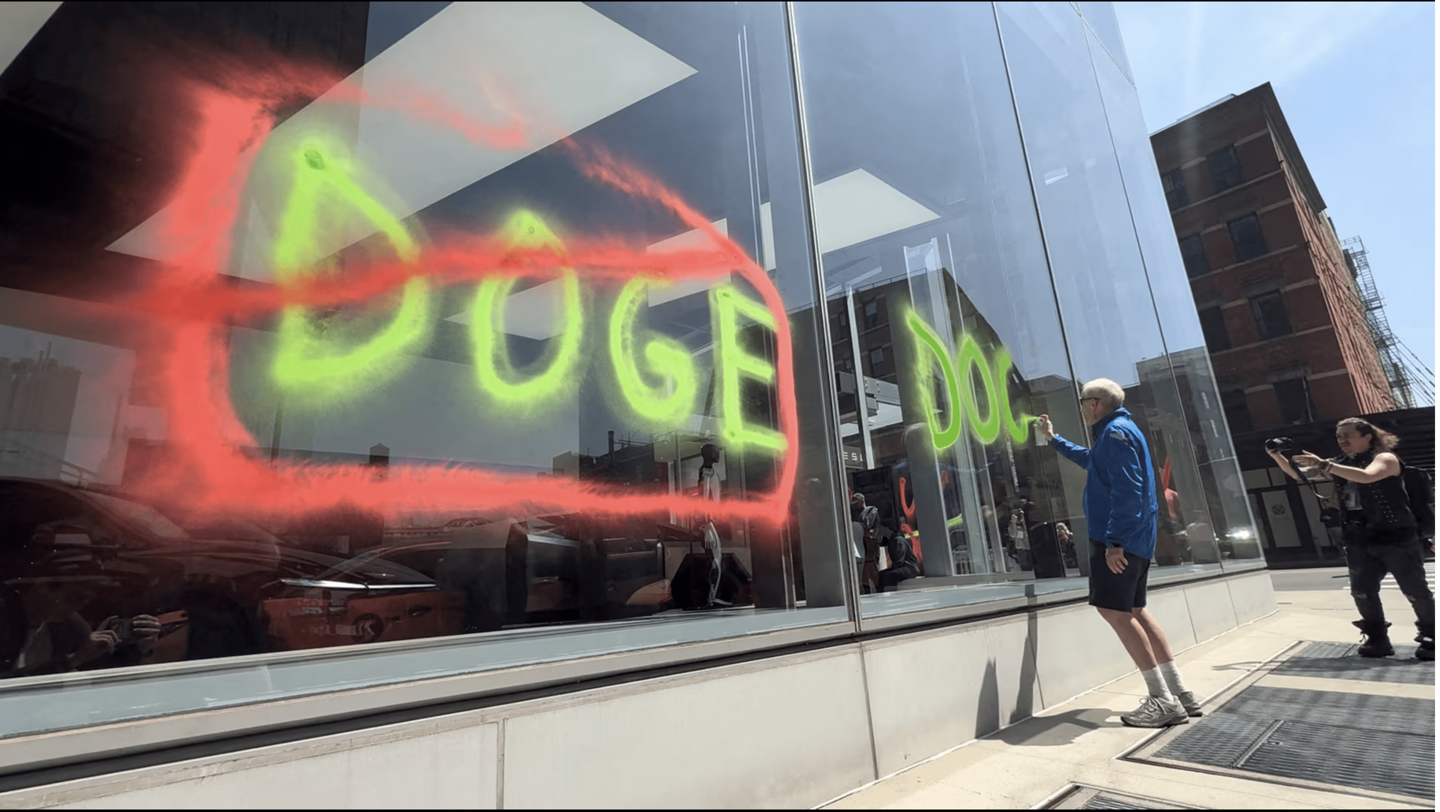 A man sprays paint graffiti against Elon Musk's Department of Government Efficiency (DOGE) on a Tesla showroom in New York, U.S., April 22, 2025, in this still image taken from video. Extinction Rebellion NYC/Handout via REUTERS